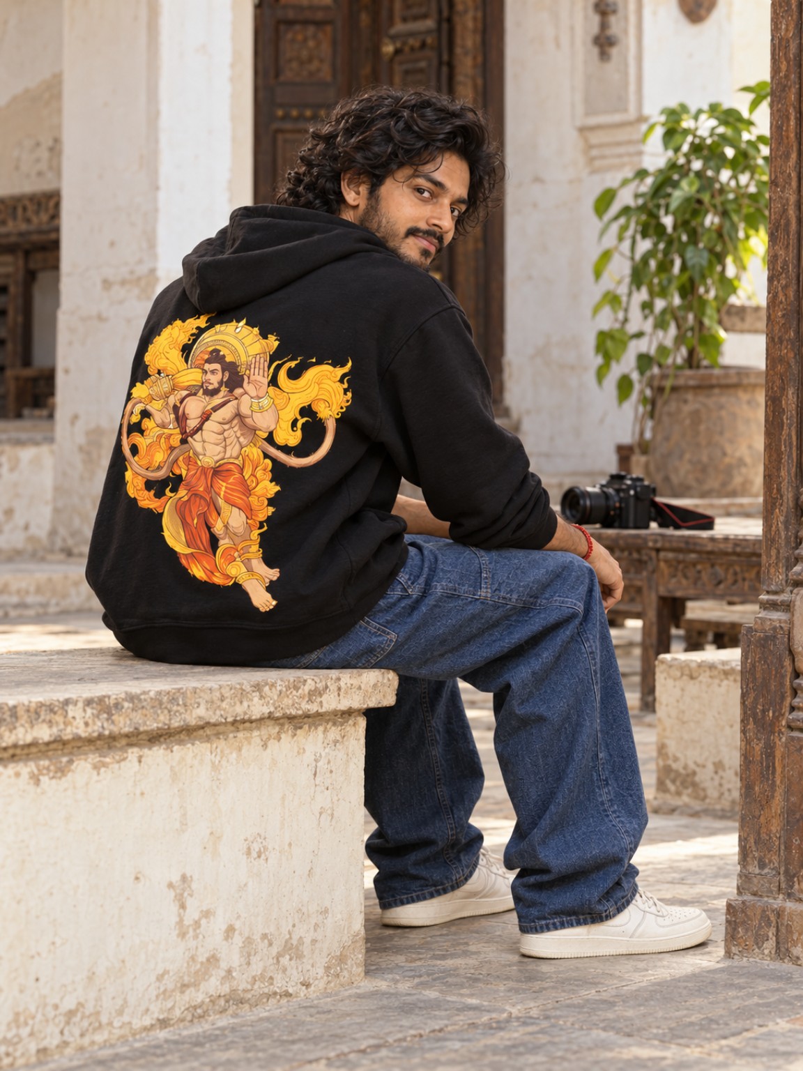 Hanumanthu seated in a courtyard wearing the black Hanuman hoodie, with his camera nearby